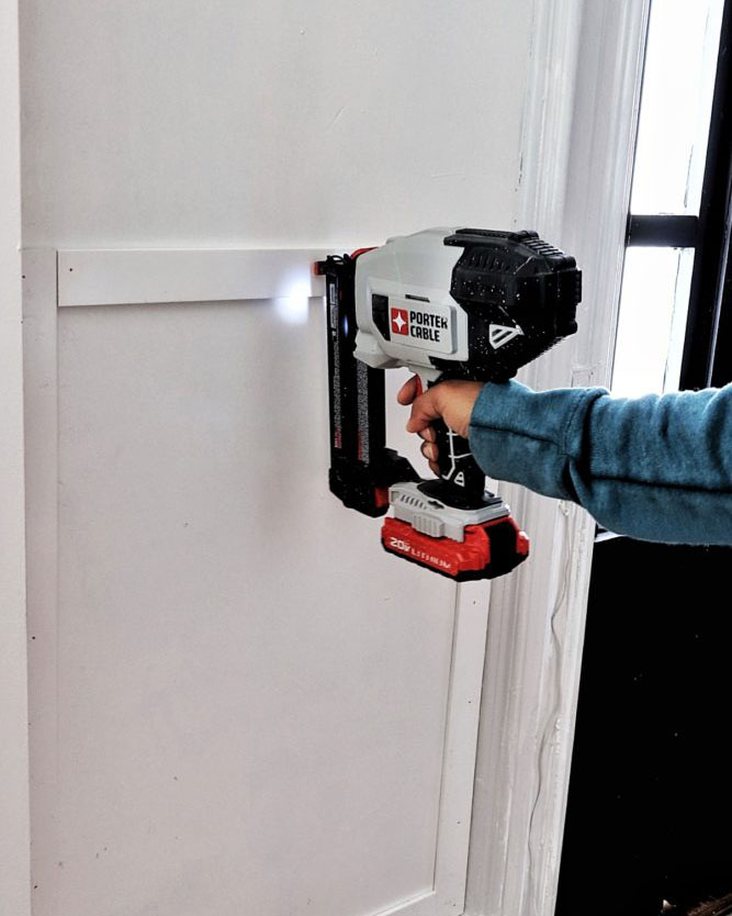 woman nailing PVC trim strips to wall with a nail gun